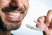 a man smiling while holding clear aligners 