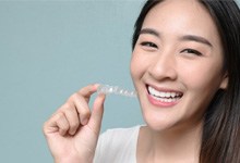 a woman smiling while holding clear aligners