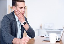 Man with watch rubbing jaw in pain 