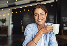 Smiling woman with dental implant tooth replacement holding a white coffee mug 