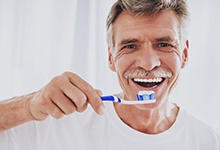 Man with dental implant tooth replacement brushing his teeth