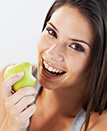 Woman with healthy smile eating an apple after preventive dentistry visit