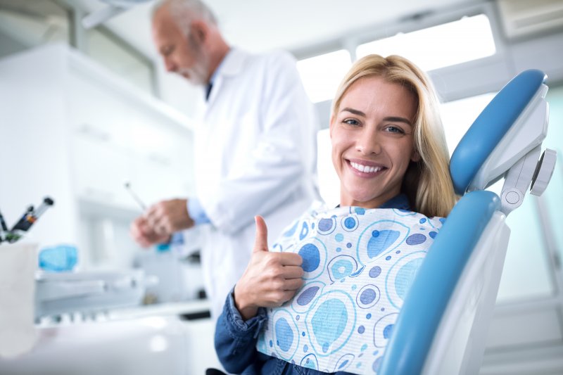 a woman smiling and giving a thumbs up in the dentist’s chair