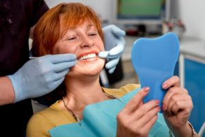 a woman smiling at her dental implants in the mirror at the dentist