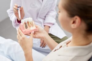Dentist gesturing to model of dental implants while patient holds model.